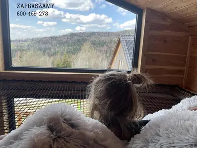 a girl laying on a bed looking out of a window at Modrzewiowe Domki w Koszarawie in Koszarawa