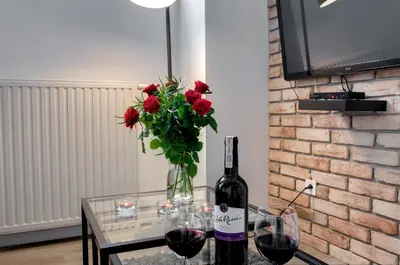 a glass table with a bottle of wine and a vase of red roses at Apartament Romantyczny Zamkowa15 in Kraków