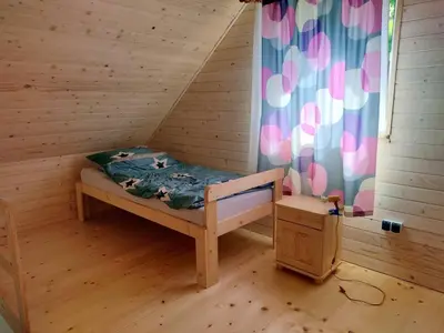 a small bed in a wooden room with a curtain at Domek Na Przełęczy in Wierzbanowa