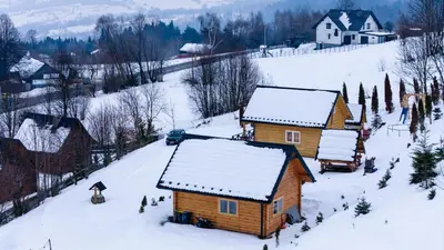 a log cabin with snow on the roof in a snow covered village at Domek Na Przełęczy in Wierzbanowa