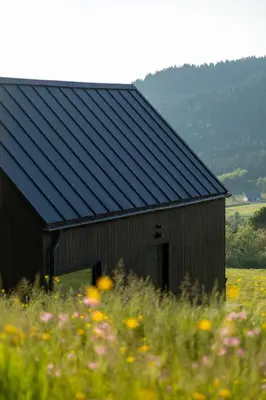 a black barn in a field of flowers at Stodoły Modyń - Domki w Beskidzie Wyspowym - staw kąpielowy, balia, sauna, grota solna - widok na góry in Kamienica