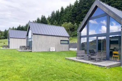 a barn with glass doors and chairs on a field at Stodoły Modyń - Domki w Beskidzie Wyspowym - staw kąpielowy, balia, sauna, grota solna - widok na góry in Kamienica
