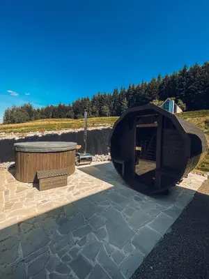 a circular wooden building with a hot tub on a patio at Stodoły Modyń - Domki w Beskidzie Wyspowym - staw kąpielowy, balia, sauna, grota solna - widok na góry in Kamienica