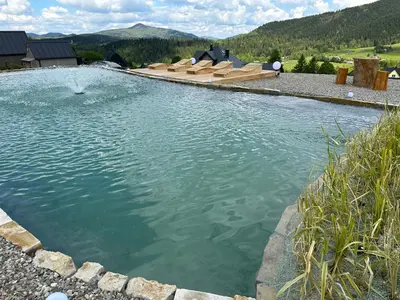 a large pool of water with benches in it at Stodoły Modyń - Domki w Beskidzie Wyspowym - staw kąpielowy, balia, sauna, grota solna - widok na góry in Kamienica