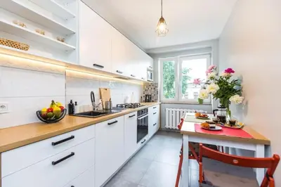 a kitchen with white cabinets and a table with a red chair at Serene Apartment in the City Center - by Upstairs in Kraków