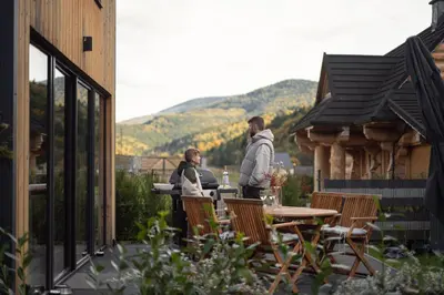 two people standing on a patio with a table and chairs at Babia Rest - całoroczny domek z balią z jacuzzi in Zawoja