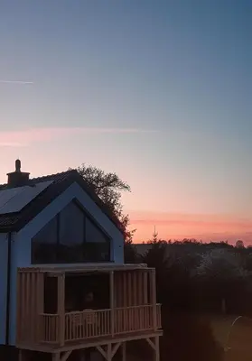 a house with a deck with the sunset in the background at Cienista Dolina in Brzoskwinia