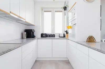 a white kitchen with white cabinets and a window at Cozy Apartment Bartla 19 by Noclegi Renters in Kraków