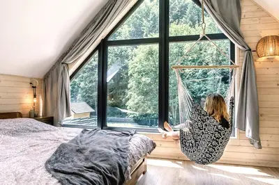a woman sitting in a hammock in a room with a window at Babia Ostoja - domek z balią i sauną in Zawoja