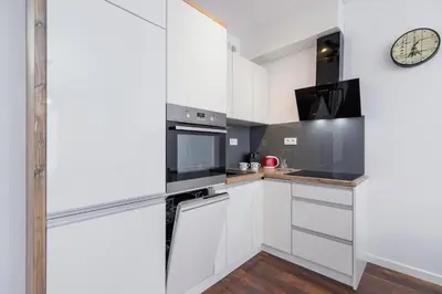 a kitchen with white cabinets and a clock on the wall at Zabłocie Pet-friendly Ślusarska Apartment by Noclegi Renters in Kraków