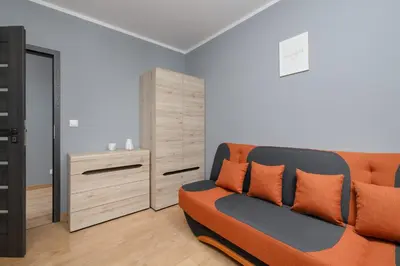 a living room with an orange couch and a dresser at Osiedle Avia Family Apartment in Kraków with Balcony by Noclegi Renters in Kraków