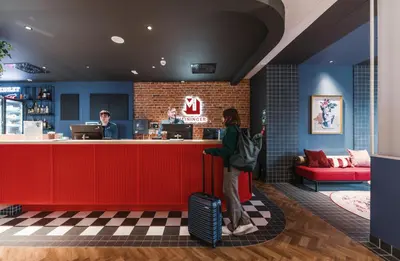a woman with a suitcase waiting at the counter of a restaurant at MEININGER Kraków Centrum in Kraków