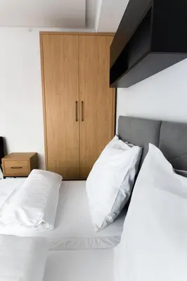 a bed with white pillows and a wooden cabinet at Apartamenty Loftove in Wadowice