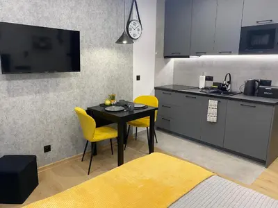 a kitchen with a table and yellow chairs and a tv at St. Cross Apartment in Kraków