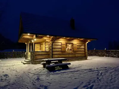a log cabin with a bench in the snow at night at Pod Gwiazdami in Dąbrówka