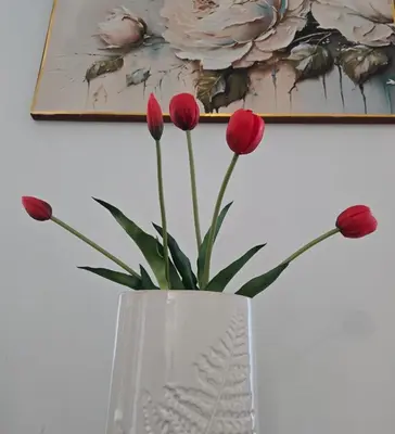 a white vase with red flowers in front of a painting at ViP APART CRACOW in Kraków