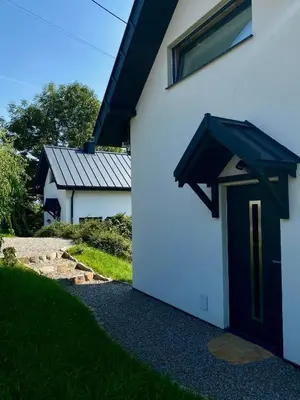 a white house with a black door and a window at Domki Na Wiosce in Stryszowa