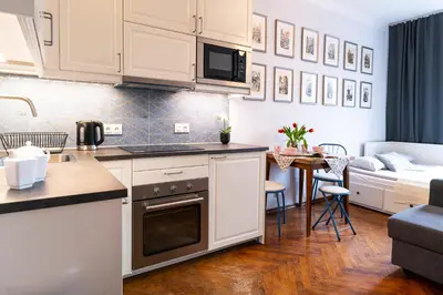a kitchen with white cabinets and a living room at Cozy Old Town Studio in Kraków