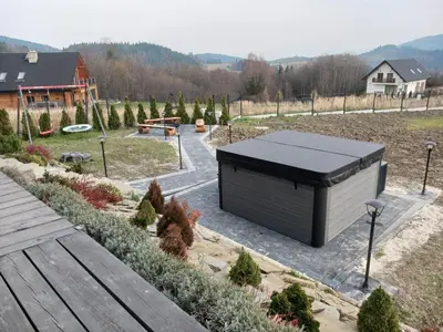 a building with a black roof in a garden at Domek w górach z balią jacuzzi Asina Chata Zawoja in Zawoja