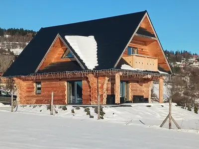 a log cabin with a black roof in the snow at Domek w górach z balią jacuzzi Asina Chata Zawoja in Zawoja