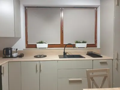 a kitchen with white cabinets and a sink and two windows at Near the airport- Apartments in Kraków