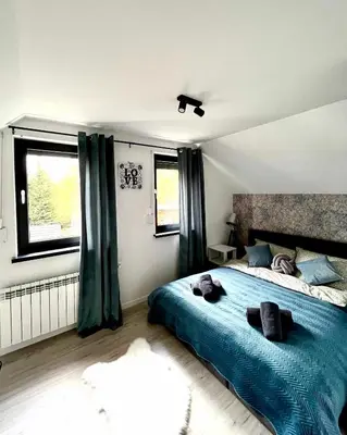 a bedroom with a bed with blue sheets and windows at Domek Leo's House in Jaszczurowa