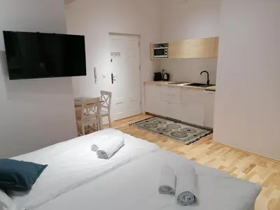 a bedroom with a white bed and a kitchen at Juwel Apartments Kraków 14 in Kraków