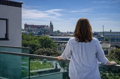 a woman standing on a balcony looking out over a city at InPoint Wawel View Apartments- Free Underground Parking in Kraków
