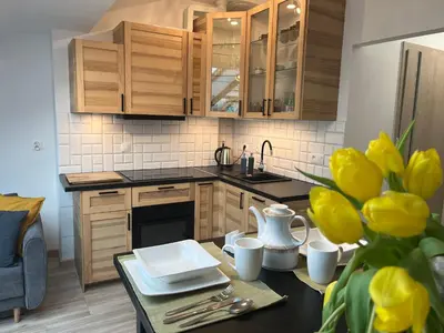 a kitchen with wooden cabinets and a table with yellow flowers at FeelHome Apartment with kitchen in Kraków