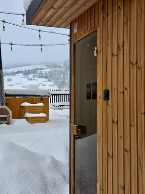 an open door of a wooden house in the snow at Gorczański Zakątek Jacuzzi & Sauna in Niedźwiedź