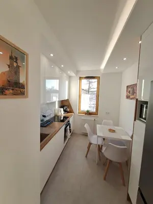 a white kitchen with a table and chairs and a counter at Apartamenty Orawska 14 HEMMA in Kraków