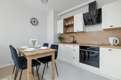 a kitchen with a wooden table and black chairs at Bright Apartment Park Lotników Near Tauron Arena Kraków by Noclegi Renters in Kraków