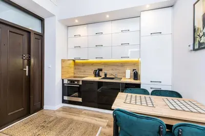 a kitchen with white cabinets and a wooden table and chairs at Nowoczesny apartament w ścisłym centrum Krakowa - by Upstairs in Kraków