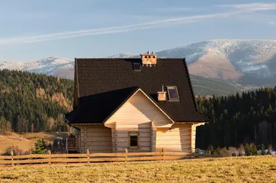 a small house in a field with mountains in the background at Domek na Zawojskim Przysłopiu in Zawoja