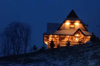 a log cabin with lights on a hill at night at Dom na Zapotoczu. Góralski dom na wyłączność na szczycie skały. in Kasinka Mala