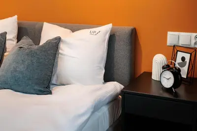 a bed with pillows and a clock on a table at Colorful Cracovia Apartments - by Upstairs in Kraków