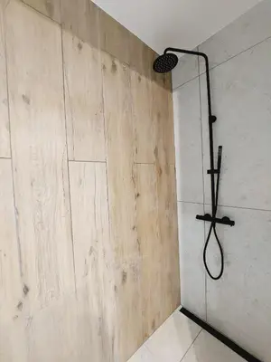 a shower in a bathroom with a wooden wall at Nowe mieszkanie Kraków, bezpłatny parking, AWG APARTMENTS in Kraków