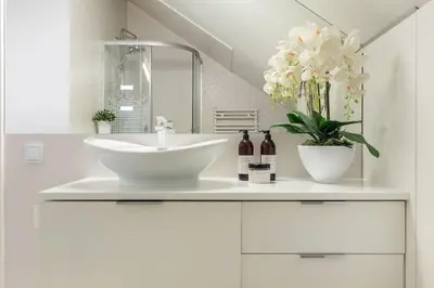 a white bathroom with a sink and flowers on a counter at MODERN & NEW place next to Wawel Castle & Vistula in Kraków
