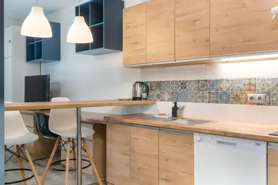 a kitchen with wooden cabinets and a counter with stools at Bronowice Standard Studio by BookingHost in Kraków