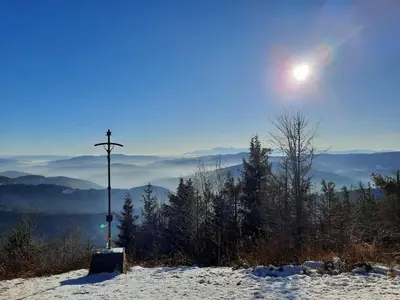 a cross on top of a snow covered hill with the sun at Mogielicki Zakątek in Jurków