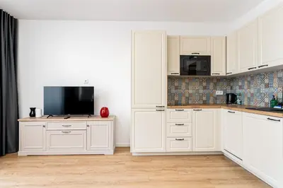 a kitchen with white cabinets and a flat screen tv at Park Zakrzówek Cosy Studio by BookingHost in Kraków