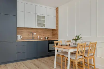 a kitchen with white cabinets and a wooden table and chairs at Cozy Apartment Orawska with Balcony by Noclegi Renters in Kraków