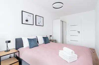 a white bedroom with a pink bed with blue pillows at Prokocim Kosocicka Apartment by BookingHost in Kraków
