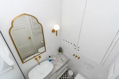 a white bathroom with a sink and a mirror at Vistula River Deluxe Apartment by BookingHost in Kraków