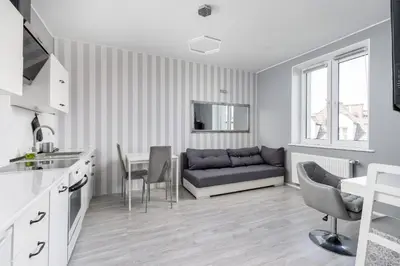 a kitchen with white cabinets and a tv on the wall at Cegielniana Grey Studio by BookingHost in Kraków