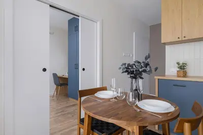 a dining room with a wooden table and a kitchen at Modern Apartment in Kraków Podgórze by Noclegi Renters in Kraków