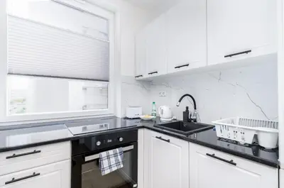a kitchen with white cabinets and a sink at Bronowice Comfy Studio by BookingHost in Kraków