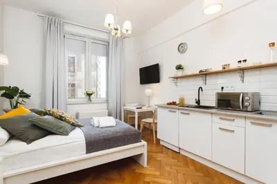 a white bedroom with a bed and a kitchen at Studio Apartment - Rzeszowska 4 Street in Kraków