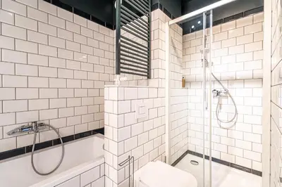 a white tiled bathroom with a shower and a tub at RentPlanet - Kamienica Retmana in Kraków