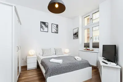 a white bedroom with a bed and a television at Charming Studio - 54 Starowislna street in Kraków